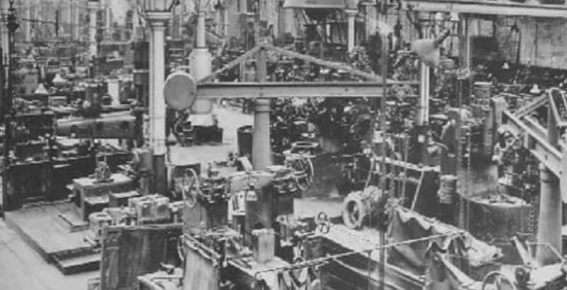 Black and white archival photo of a crowded old factory floor filled with machinery, pillars, and equipment